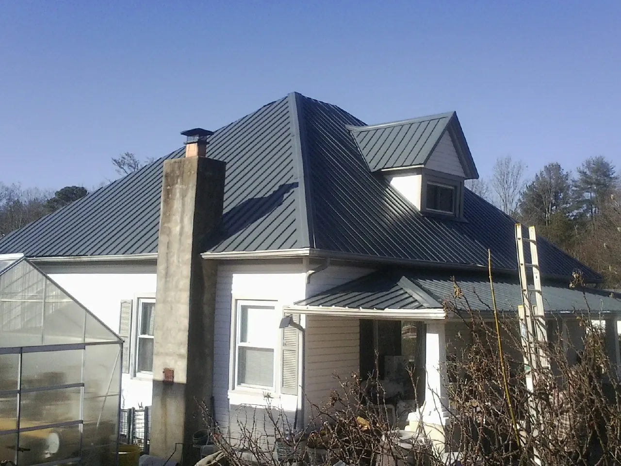 Dark blue standing seam metal roof on a white farmhouse with dormer — Slate & Tile Roof Repair by Roofing Brothers in Branson