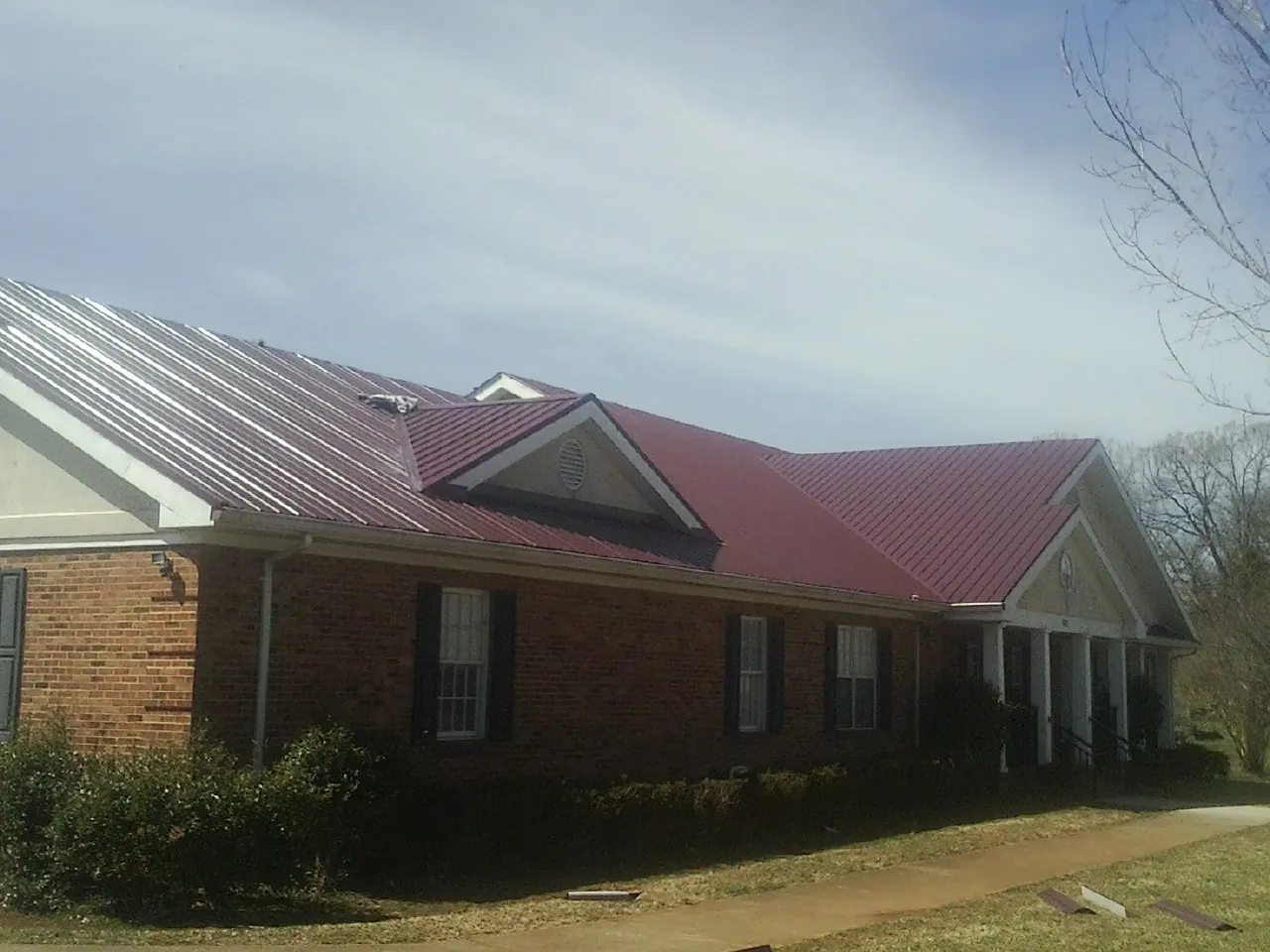 Red metal roof with gabled entries on a long brick building, from a Hail Damage Roof Repair job in Branson