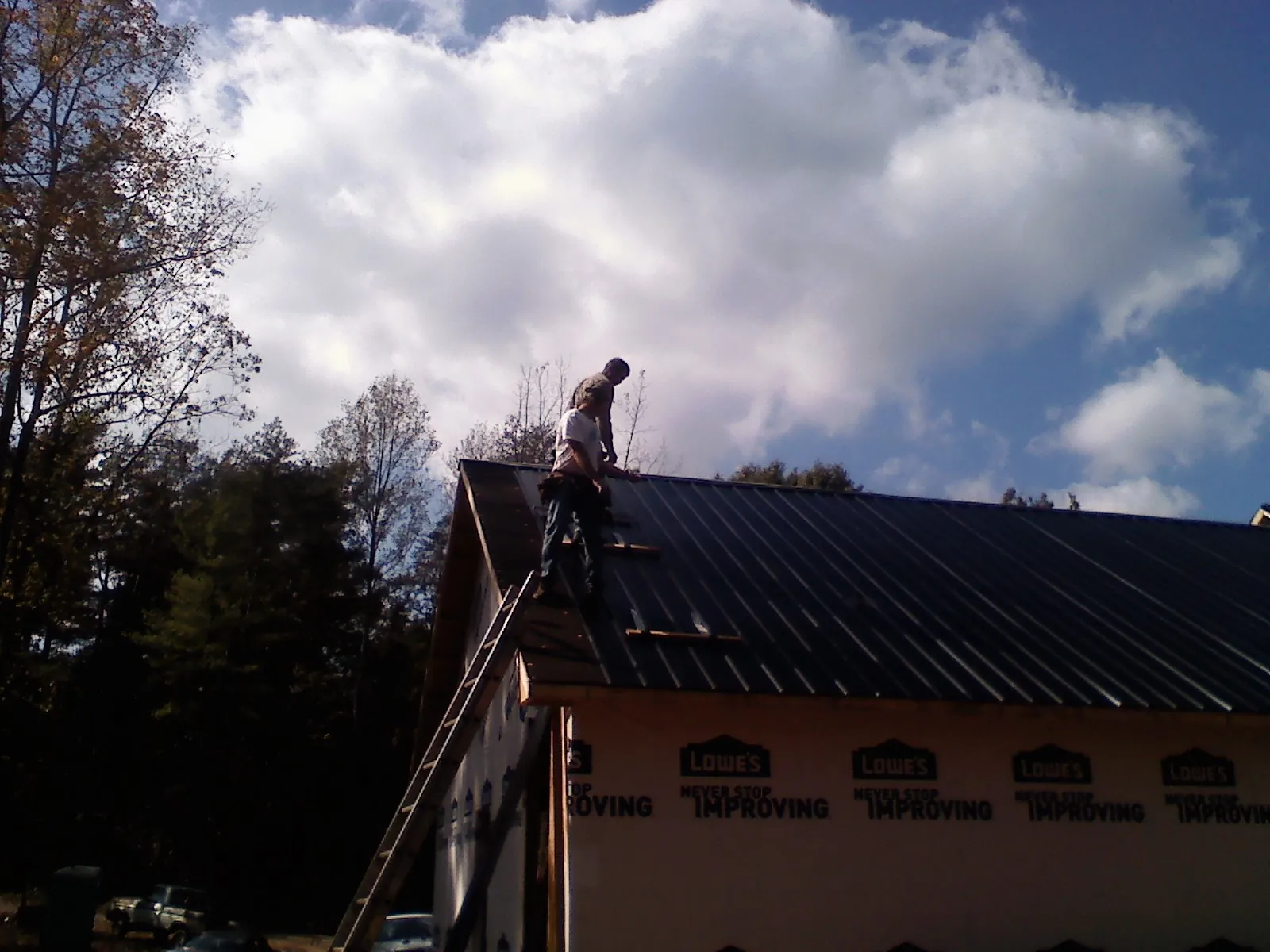 Roofer fastening dark metal panels high against a cloudy sky, from a Roof Inspection job in Branson