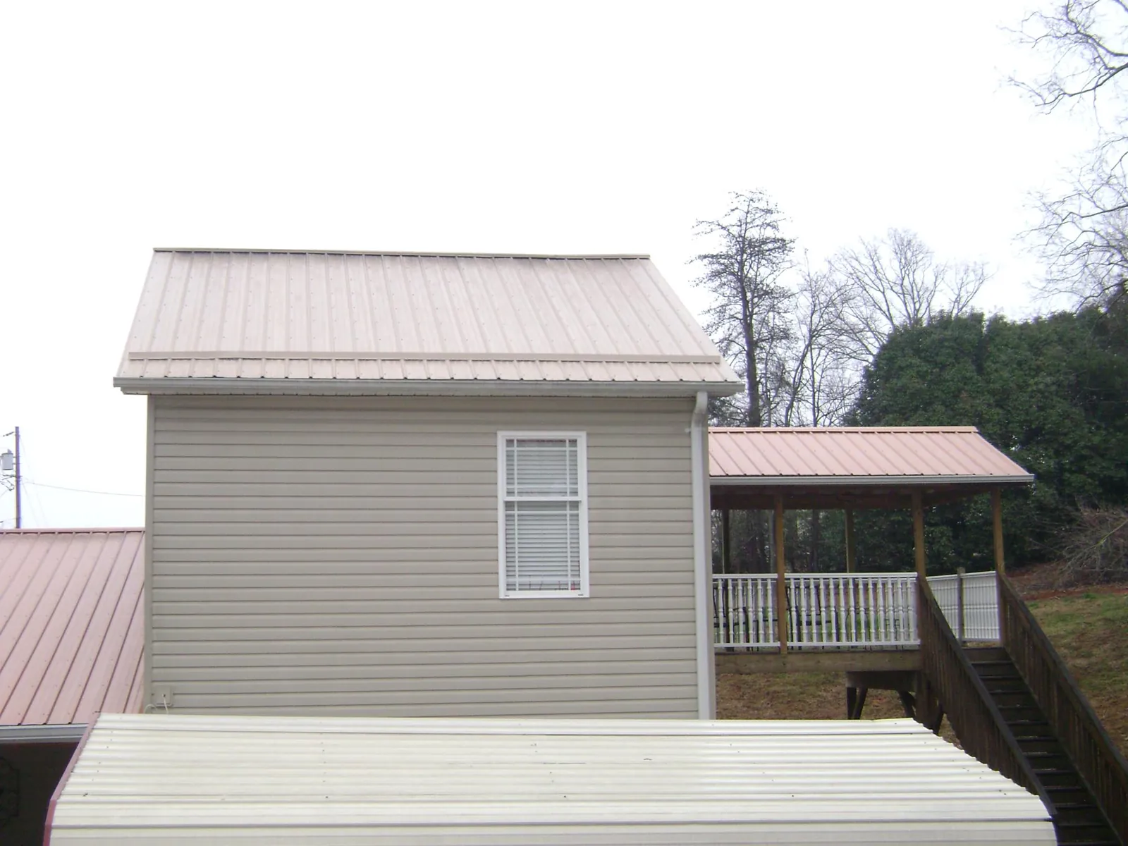 Tan metal roofs on a two story addition and attached porch, from a Roof Replacement job in Branson